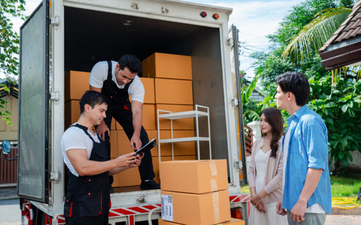 Asian Couple check while unloading boxes and furniture from a pickup truck to a new house with service cargo two men movers worker in uniform lifting boxes. concept of Home moving and delivery.